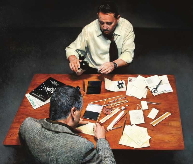 两个男人面对面坐在一张散落着文件和其他物品的木桌旁。