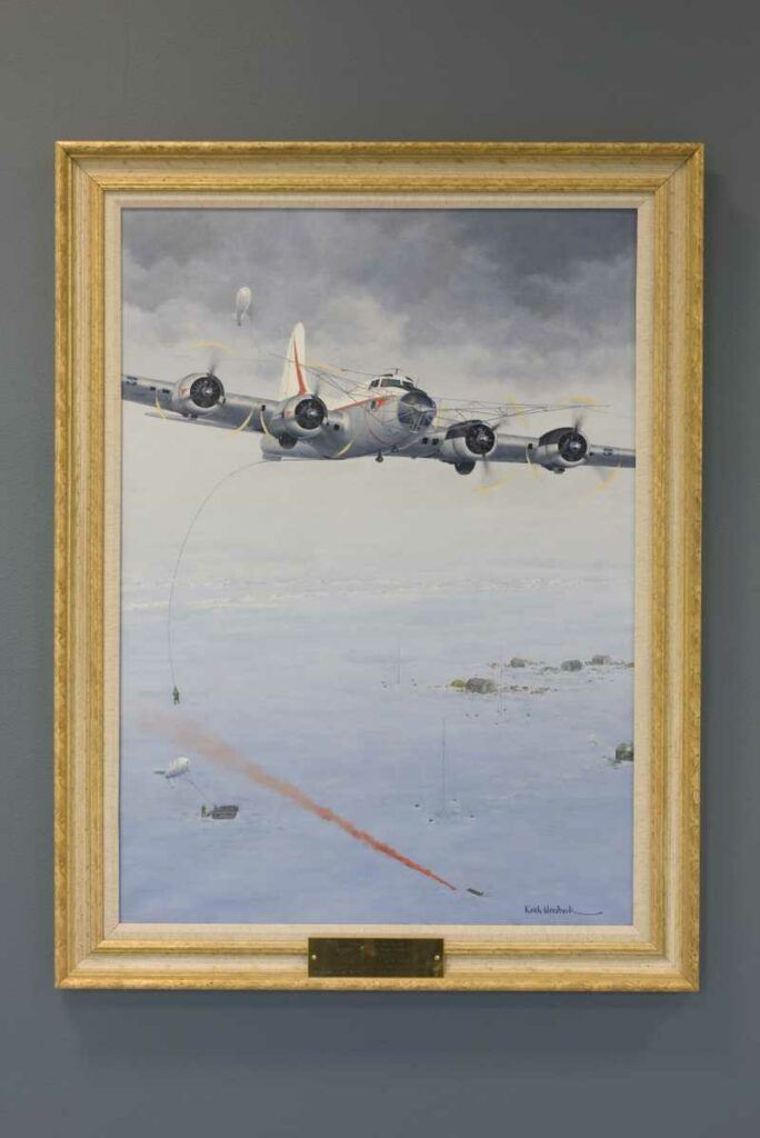一幅带框的油画，描绘了一架 B-17 试图接起两名美国士兵，其中一名还在红色照明弹旁边的地上